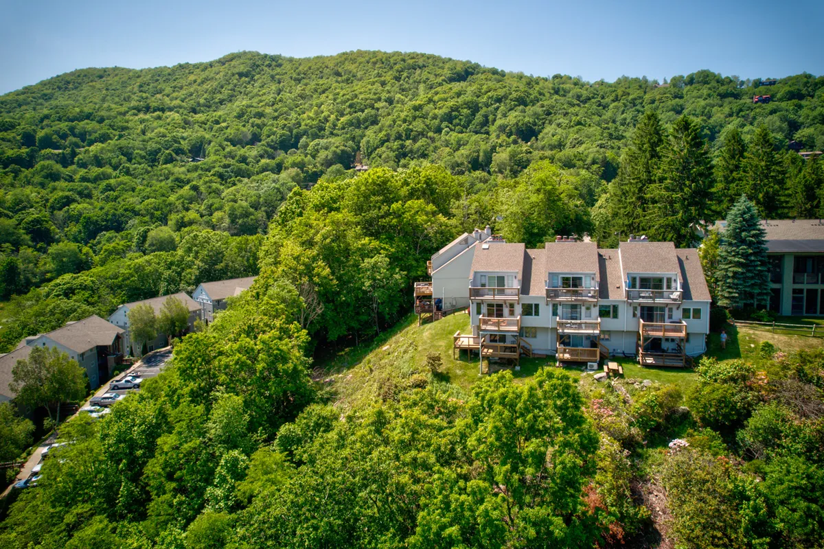 Multi-level residential buildings are nestled among lush greenery, with a stunning mountain backdrop. The architecture hints at a mountain lodge ambiance and the proximity to adventure-filled landscapes.