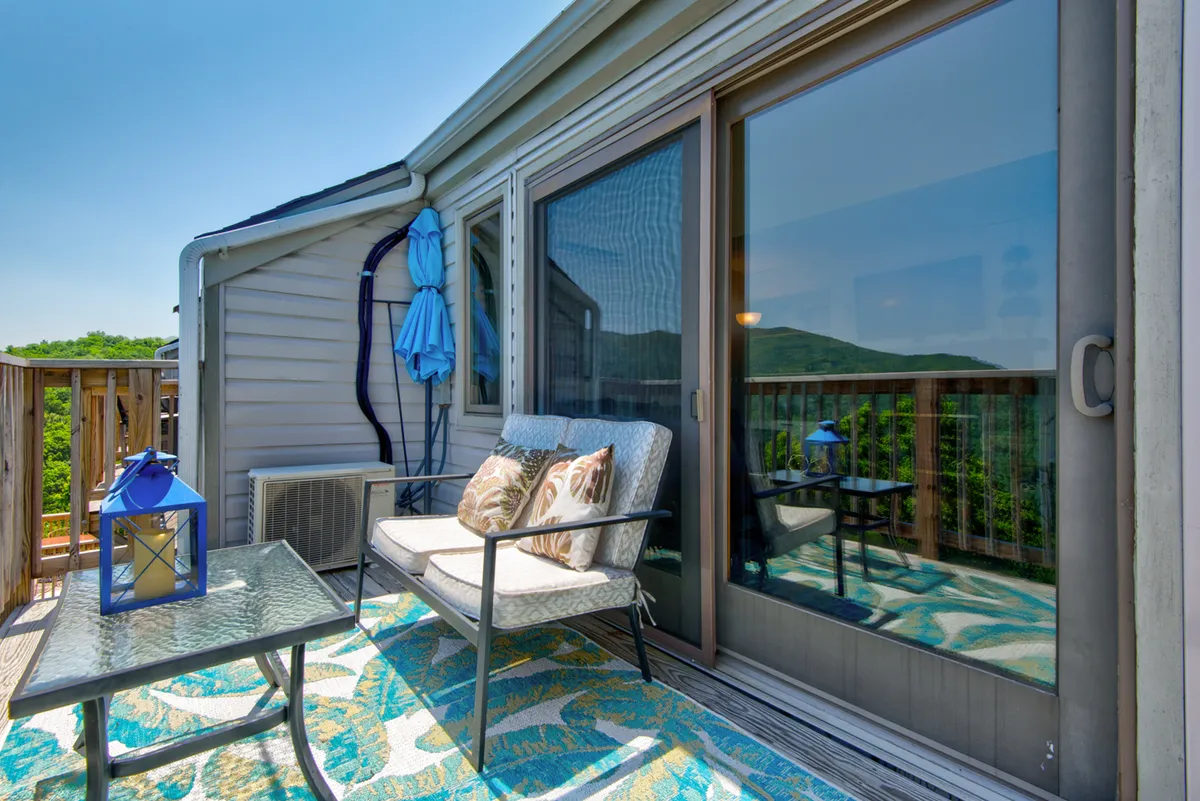 A welcoming outdoor seating area with comfortable chairs, a decorative rug, lantern, and a blue umbrella. The arrangement invites guests to unwind outside, enjoy the view, or socialize in a tranquil setting.
