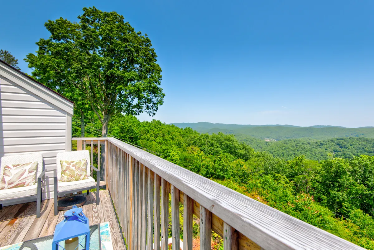 A tranquil wooden deck with comfortable chairs overlooks lush greenery and distant mountains. The space is ideal for morning coffee or evening stargazing, offering expansive views and an intimate spot for couples to share quiet time surrounded by nature.