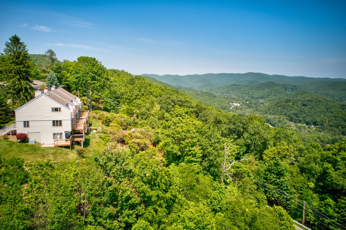 A wide exterior shot showing homes perched on a hillside, surrounded by vibrant green grass and distant, layered mountain ranges. The scene conveys a sense of adventure and proximity to nature, suggesting easy access to hiking and outdoor exploration. Outdoor living spaces invite relaxation after a day out.