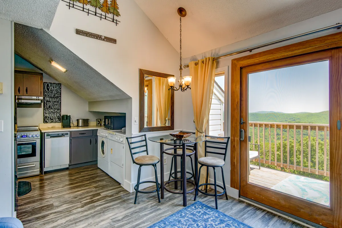 This image features a cozy and inviting kitchen and dining area, with modern appliances, a welcoming dining table, and large windows that offer scenic views. The space is filled with natural light, enhancing its open-plan layout, and creating an ideal environment for cooking and enjoying meals together.